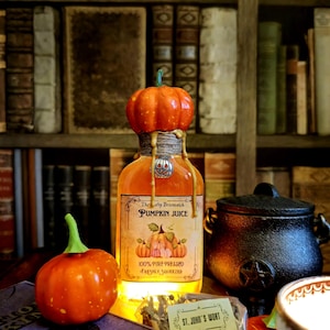 Könnte beinhalten: Eine Glasflasche mit einem Kürbis-Stopfen, gefüllt mit einer goldenen Flüssigkeit. Die Flasche trägt ein Etikett mit der Aufschrift "The afty Broomstick Pumpkin Juice 100% Pure Pressed Freshly Squeezed". Im Vordergrund befinden sich ein kleiner Kürbis und ein Beutel mit Kräutern, der mit "St. John's Wort" beschriftet ist.