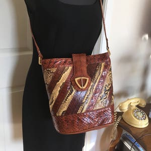 May include: A brown leather shoulder bag with a snakeskin pattern. The bag has a gold-toned buckle and a long strap.