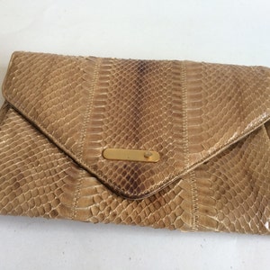 Peut inclure: Une pochette en cuir de serpent beige avec un fermoir doré.