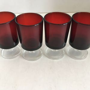 May include: Four clear glass shot glasses with a red base and a clear stem. The glasses are arranged in a row.