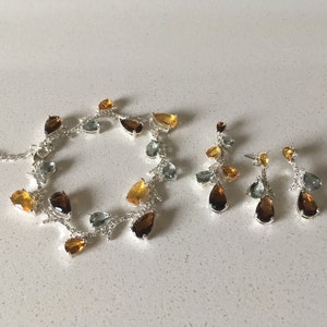 May include: A silver necklace and earrings set with teardrop-shaped gemstones in shades of amber, brown, and green.