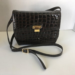 May include: A brown crocodile-embossed leather shoulder bag with a gold-toned clasp.