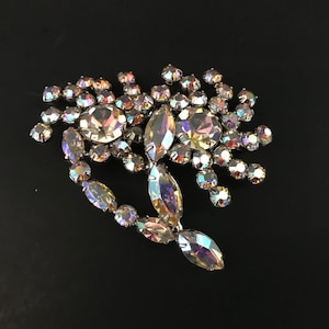May include: A large iridescent rhinestone brooch in the shape of a flower with a long, pointed leaf extending from the bottom.