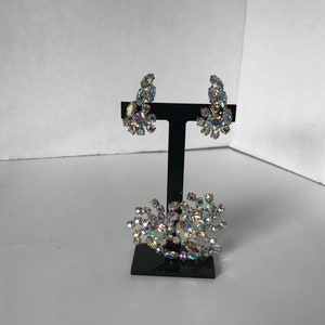 May include: A set of iridescent rhinestone earrings and a brooch. The earrings are clip-on style and the brooch is a cluster of rhinestones.