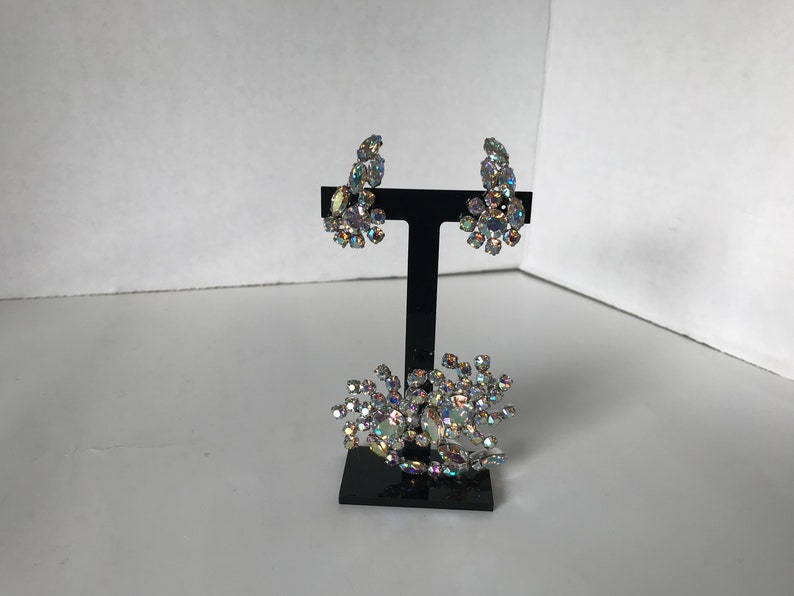 May include: A set of iridescent rhinestone earrings and a brooch. The earrings are clip-on style and the brooch is a cluster of rhinestones.