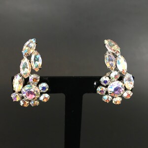 May include: A pair of iridescent crystal earrings with a silver tone setting. The earrings are shaped like a cluster of crystals.