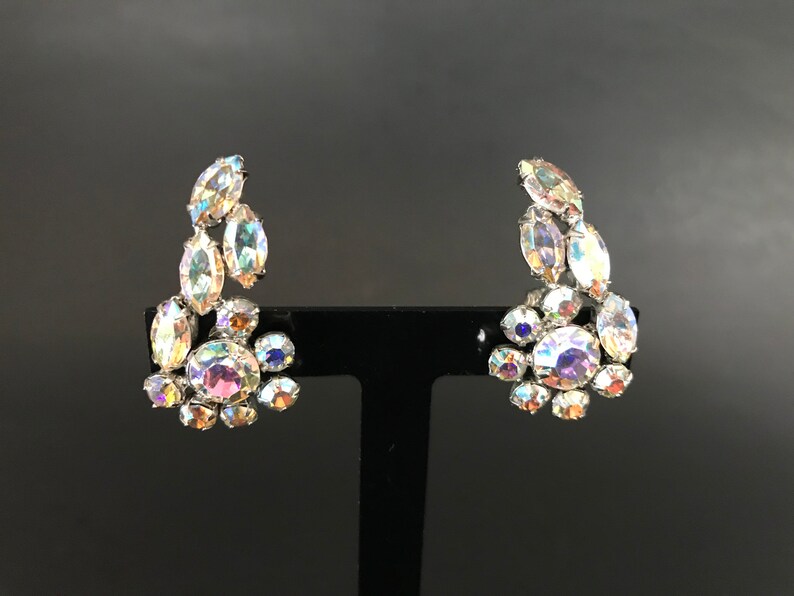May include: A pair of iridescent crystal earrings with a silver tone setting. The earrings are shaped like a cluster of crystals.