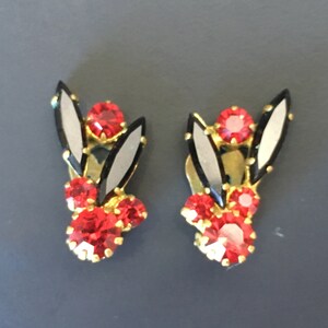 Peut inclure: Une paire de boucles d'oreilles clips avec un motif en émail noir et blanc et des strass rouges.