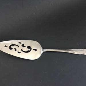 May include: A silver cake server with a decorative, cut-out design on the blade. The handle is ornate and has a scalloped edge.