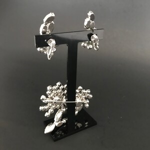 May include: A pair of silver clip-on earrings with a cluster of clear rhinestones. The earrings are displayed on a black stand.