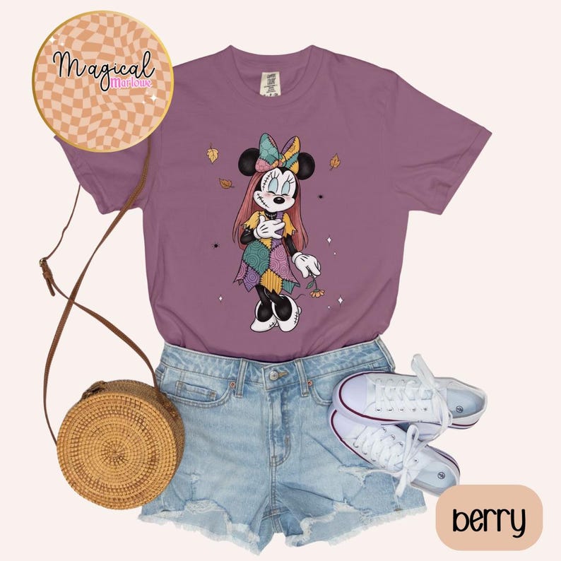 Pu&ograve; includere: T-shirt color bacca con grafica di Minnie Mouse in un abito patchwork. L'immagine include pantaloncini di jeans, scarpe da ginnastica bianche e una borsa a tracolla intrecciata. La maglietta ha girocollo e maniche corte. Il testo "Magical Midlouse" &egrave; in un cerchio in alto a sinistra.
