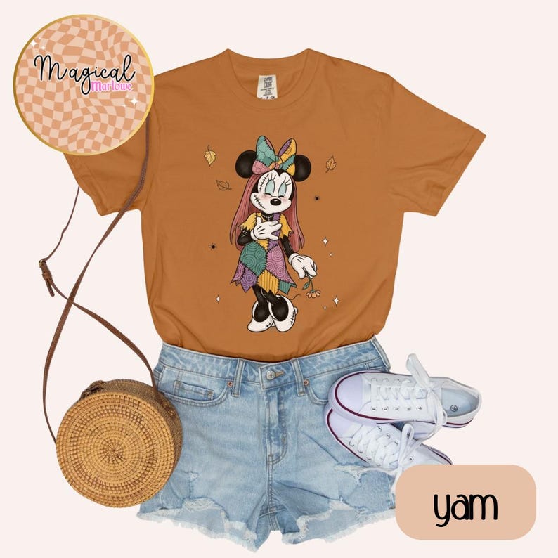 Pu&ograve; includere: Una maglietta color igname con una grafica di Minnie Mouse in un vestito patchwork. L'immagine include pantaloncini di jeans, scarpe da ginnastica bianche e una borsa a tracolla intrecciata. Il testo "Magical Marlowe" &egrave; in un design circolare.
