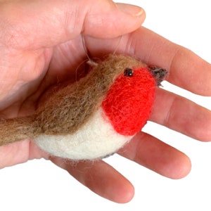 May include: A small, hand-felted robin ornament with a red breast, brown back, and white belly. The ornament is held in a hand, showing its size and detail.