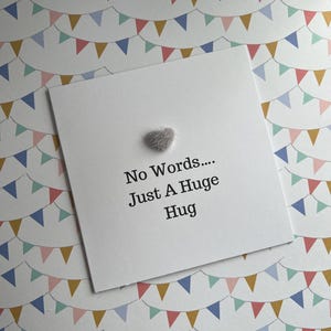May include: A white card with the message "No Words.... Just A Huge Hug" and a small, grey, fluffy heart. The background features a pattern of colourful triangular bunting flags.