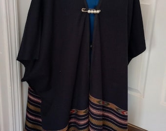 May include: A black shawl with a colorful woven border and fringe. The shawl is fastened with a silver safety pin.