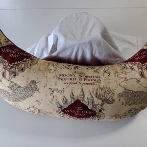 May include: A crescent-shaped pillow with a beige background and a red and black print of the Marauder's Map from the Harry Potter series. The map features the text "Messrs. Moony Wormtail Padfoot & Prongs are proud to present The Marauder's Map."