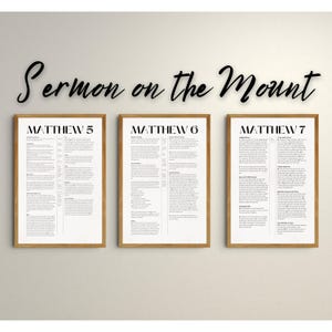 Puede incluir: Tres impresiones enmarcadas con el texto "Sermón de la Montaña" en la parte superior. Cada impresión presenta el texto "Mateo" seguido de un número 5, 6 o 7. Las impresiones están en una pared blanca.