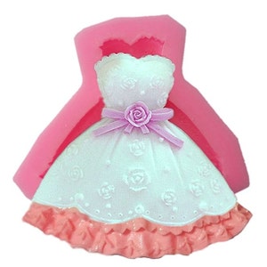 May include: Pink silicone mould shaped like a white dress with a pink bow and a pink rose. The dress has a lace pattern and a ruffled bottom.