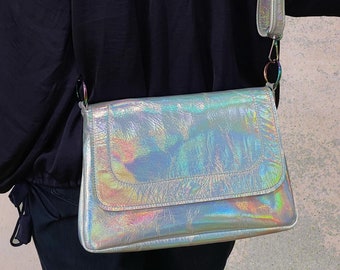 May include: A rectangular crossbody bag with a metallic, iridescent finish that reflects rainbow colours. The bag features a fold-over flap, a smooth texture, and an adjustable shoulder strap attached with silver-toned metal rings on both sides.