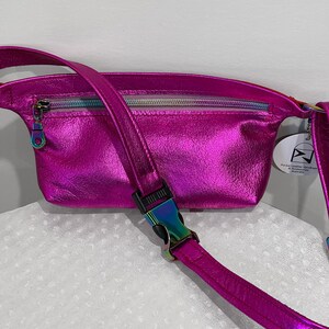 Puede incluir: Una ri&ntilde;onera de cuero iridiscente rosa brillante con un bolsillo con cremallera y una correa ajustable con una hebilla plateada. La bolsa tiene una peque&ntilde;a etiqueta que dice "Pure Leather Handbags & Accessories Australia".
