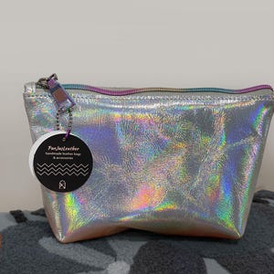 May include: A silver holographic leather pouch with a rainbow zipper and a tag that reads "FunJustLeather handmade leather bags & accessories". The pouch is sitting on a gray patterned surface.