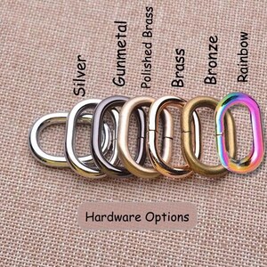May include: A collection of six oval metal rings arranged in a row, labeled Hardware Options. The finishes include silver, gunmetal, polished brass, brass, bronze, and a multi-colored rainbow finish. Each ring features a smooth, rounded surface.