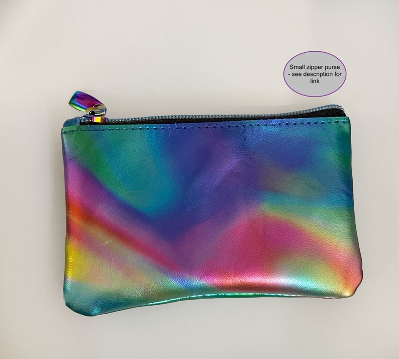 May include: A small rectangular zipper purse with a metallic iridescent finish featuring a spectrum of colors including blue, green, purple, and pink. The purse has a black zipper closure and includes the text Small zipper purse - see description for link.