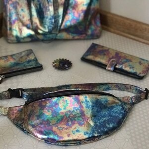 Puede incluir: Un conjunto de bolsos iridiscentes de varios tama&ntilde;os, que incluyen un bolso de mano, una cartera, una peque&ntilde;a bolsa y una ri&ntilde;onera. Todos los bolsos est&aacute;n hechos de un material brillante e iridiscente con un patr&oacute;n de arco&iacute;ris.
