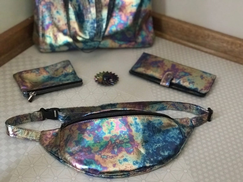 Puede incluir: Un conjunto de bolsos iridiscentes de varios tama&ntilde;os, que incluyen un bolso de mano, una cartera, una peque&ntilde;a bolsa y una ri&ntilde;onera. Todos los bolsos est&aacute;n hechos de un material brillante e iridiscente con un patr&oacute;n de arco&iacute;ris.