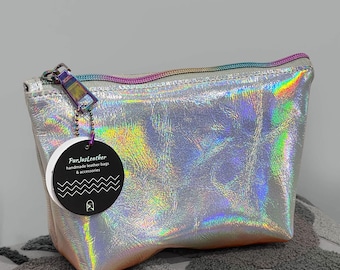 May include: A holographic silver pouch with a textured surface and a rainbow-colored zipper. A round black tag attached to the zipper pull features the white text PurJusLeather handmade leather bags & accessories and a small icon.