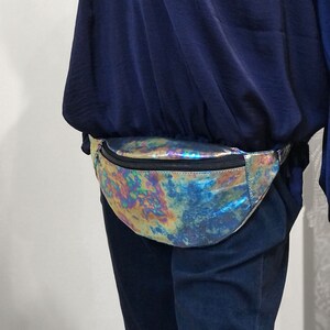 Puede incluir: Una ri&ntilde;onera hologr&aacute;fica iridiscente con cierre de cremallera. La ri&ntilde;onera se lleva alrededor de la cintura de una persona que lleva una camisa azul y pantalones azul oscuro.