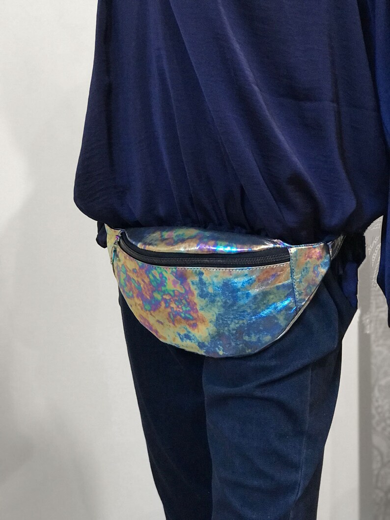 Puede incluir: Una ri&ntilde;onera hologr&aacute;fica iridiscente con cierre de cremallera. La ri&ntilde;onera se lleva alrededor de la cintura de una persona que lleva una camisa azul y pantalones azul oscuro.