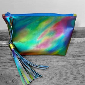 Puede incluir: Una bolsa de cosm&eacute;ticos iridiscente azul, verde y rosa con una cremallera azul y un borla a juego.