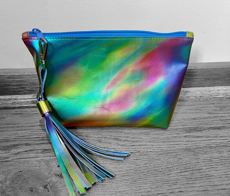 Puede incluir: Una bolsa de cosm&eacute;ticos iridiscente azul, verde y rosa con una cremallera azul y un borla a juego.