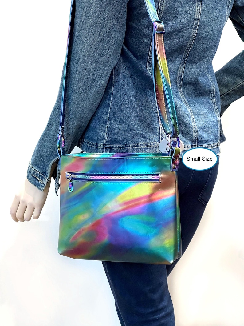 May include: A small iridescent rainbow crossbody bag with a zipper closure. The bag has a long adjustable strap and is made of a shiny, holographic material. "Small Size" is written on a white tag attached to the bag.