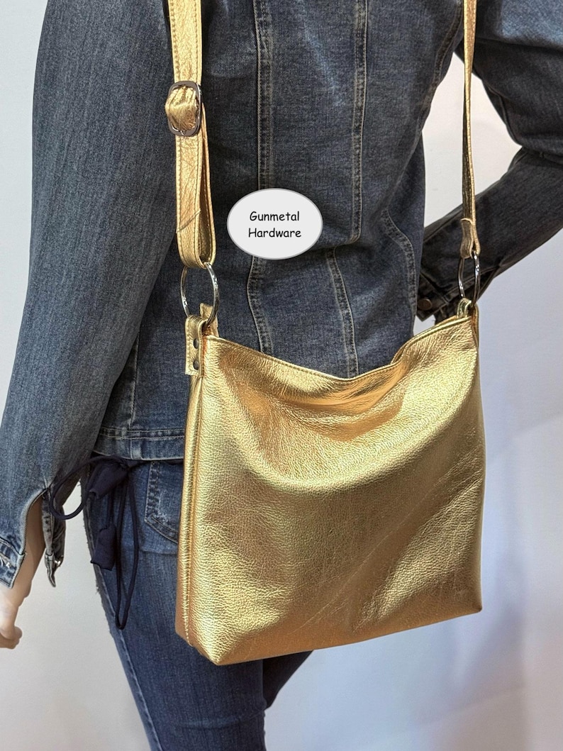 Puede incluir: Un bolso de hombro dorado con una correa larga y herrajes de metal pavonado. El bolso tiene forma rectangular y un aspecto suave y texturizado. El texto "Gunmetal Hardware" es visible en la imagen.