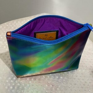 Puede incluir: Una peque&ntilde;a bolsa de cremallera iridiscente azul, verde y rosa con forro morado. La bolsa tiene una etiqueta de cuero con el texto "Purse+Leather".