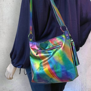 May include: A crossbody bag with a metallic, iridescent finish that shifts between shades of green, blue, purple, and yellow. The bag features a long adjustable shoulder strap, a horizontal zippered pocket on the front, and a decorative tassel.