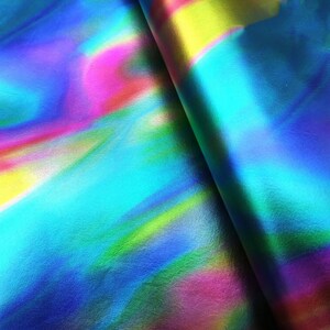 May include: A sheet of synthetic material featuring a vibrant holographic finish with a smooth, reflective surface. The colors shift between bright shades of cyan, magenta, yellow, and deep blue in a fluid, abstract pattern across the entire area.