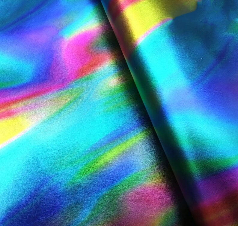 May include: A sheet of synthetic material featuring a vibrant holographic finish with a smooth, reflective surface. The colors shift between bright shades of cyan, magenta, yellow, and deep blue in a fluid, abstract pattern across the entire area.