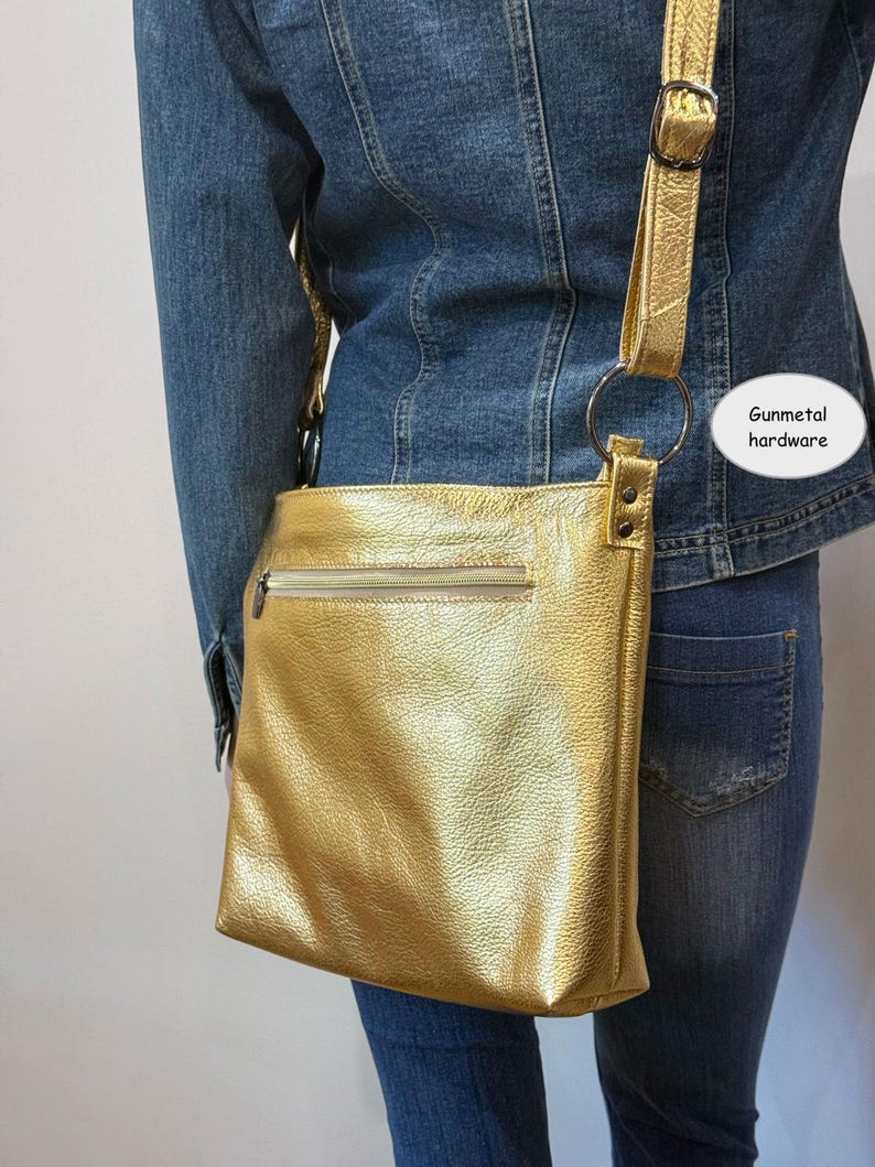 Puede incluir: Un bolso bandolera dorado con cierre de cremallera y correa ajustable. El bolso presenta herrajes de metal de ca&ntilde;&oacute;n y una superficie texturizada. El bolso se lleva sobre una chaqueta vaquera y unos vaqueros.