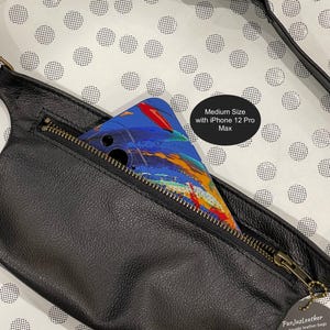 Puede incluir: Una ri&ntilde;onera de cuero negro con cierre de cremallera y tirador de cremallera dorado. Se puede ver un tel&eacute;fono inteligente dentro de la bolsa. La bolsa est&aacute; sobre un fondo blanco con lunares negros. El texto "Medium Size with iPhone 12 Pro Max" es visible en la imagen. El texto "Pur JusLeather handmade leather bags & accessories" es visible en una etiqueta negra con un patr&oacute;n de zigzag blanco.