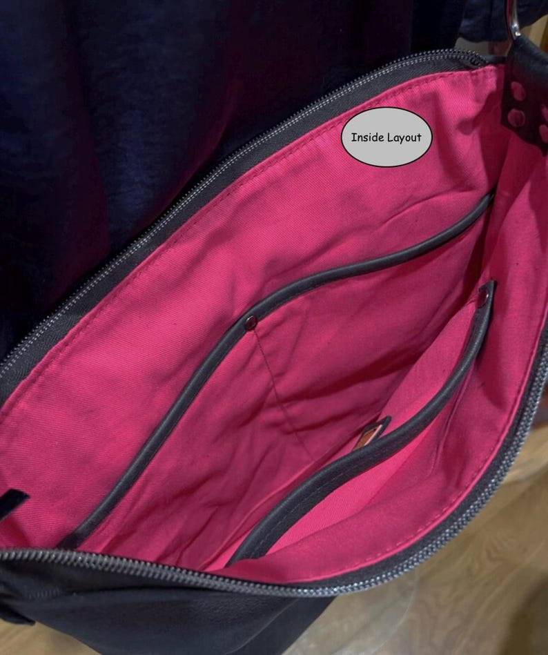 May include: A black bag with a vibrant pink interior lining. The bag features a top zipper closure and multiple internal pockets with dark gray trim. A small oval label with the text Inside Layout is visible near the top of the pink fabric.
