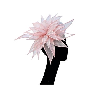 Op de afbeelding: Een roze hoed in de vorm van een bloem, gemaakt van delicate stof. De hoed is ontworpen met een grote, gelaagde bloem die een volumineuze en elegante uitstraling cre&euml;ert.