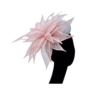 Op de afbeelding: Een roze en witte fascinator met een groot, gelaagd bloemmotief. De bloem is gemaakt van een delicate, doorschijnende stof en heeft een gerimpelde textuur.