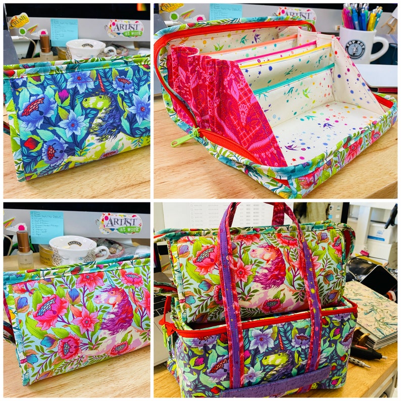 May include: A set of three colorful fabric storage bags with a floral and unicorn print. The bags are zippered and have handles. The largest bag has a removable insert with multiple compartments. The bags are labeled "Artist at Work".