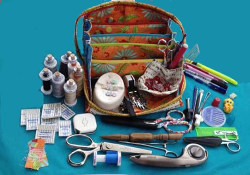 May include: A colorful fabric sewing kit with multiple compartments, filled with sewing supplies including spools of thread, needles, scissors, and a rotary cutter.