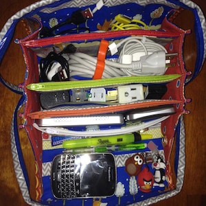 May include: A blue and gray fabric bag with multiple compartments. The bag is filled with various cords, plugs, and a small black phone. The phone has the text "Blackberry" on the front.