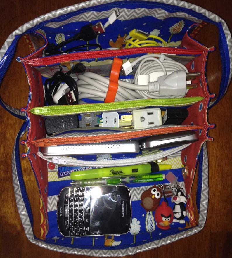 May include: A blue and gray fabric bag with multiple compartments. The bag is filled with various cords, plugs, and a small black phone. The phone has the text "Blackberry" on the front.
