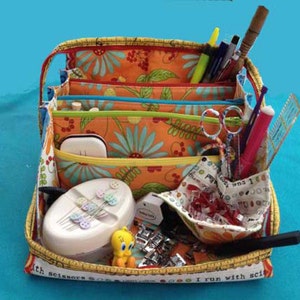 May include: A multi-colored fabric storage tote with multiple compartments. The tote is filled with sewing supplies, including scissors, needles, thread, and buttons. The tote has a yellow and white tape measure around the edge with the text "I run with scissors".